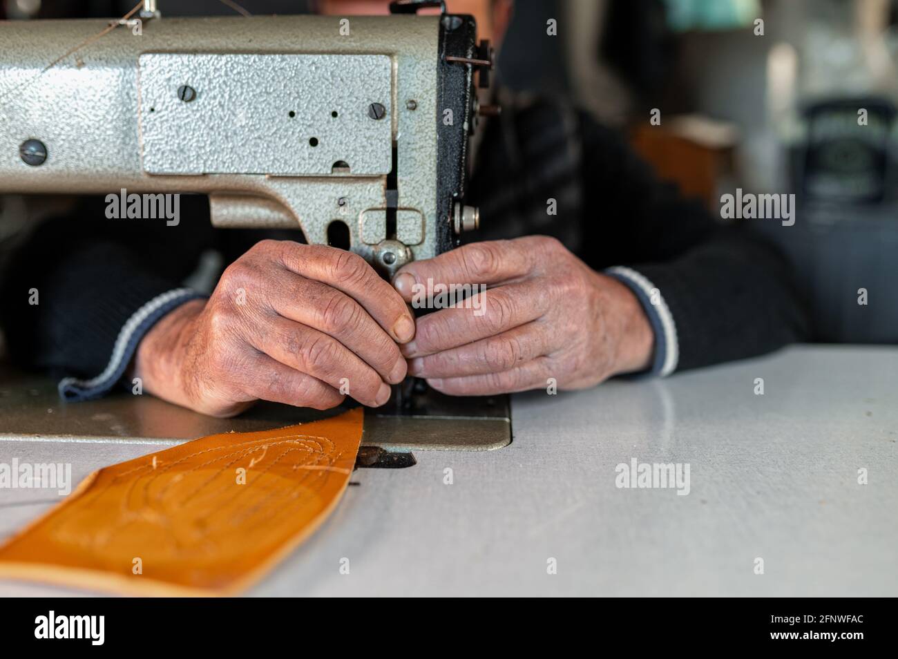 Gros plan des mains de hommes âgés mettant en place une machine à coudre travaillant avec du cuir. Concept de savoir-faire. Banque D'Images