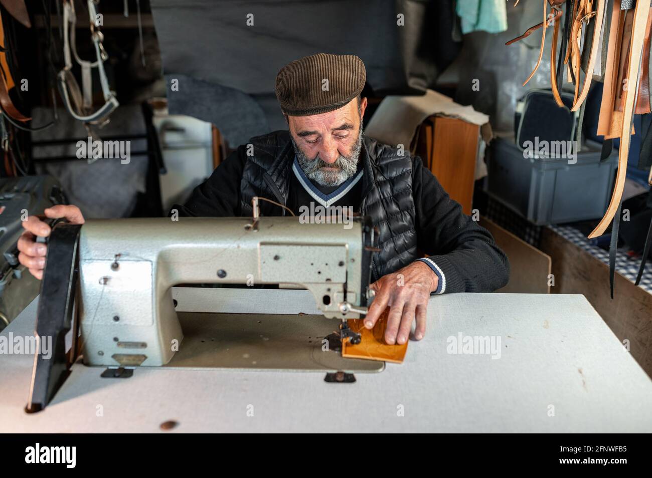 Homme barbu de hipster ancien avec une casquette plate travaillant avec machine à coudre et cuir Banque D'Images