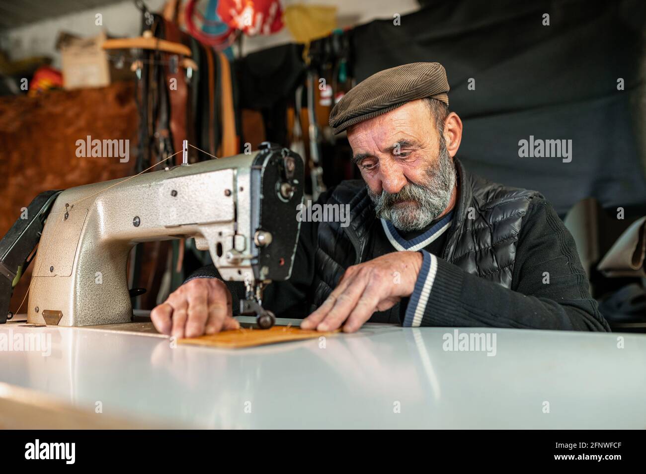 Vieil homme barbu avec casquette plate travaillant avec du cuir à l ...