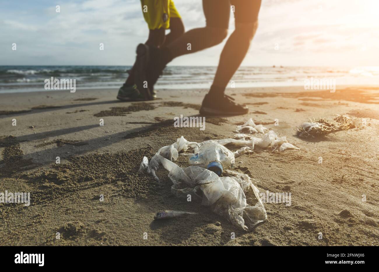 Les déchets en plastique et les jambes de personnes sur la plage avec éclairage extérieur au soleil. Banque D'Images
