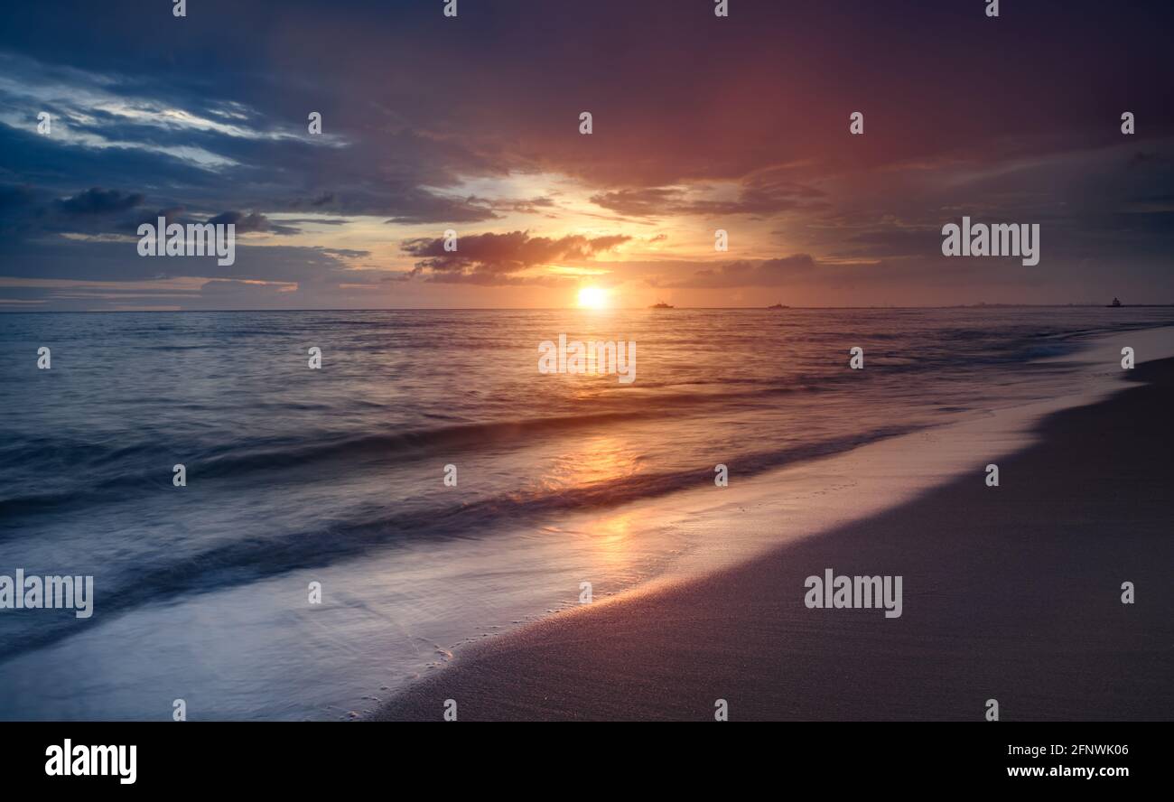 Coucher de soleil sur la plage avec une longue exposition, vague douce et floue avec une ombre sombre peu éclairée. Banque D'Images