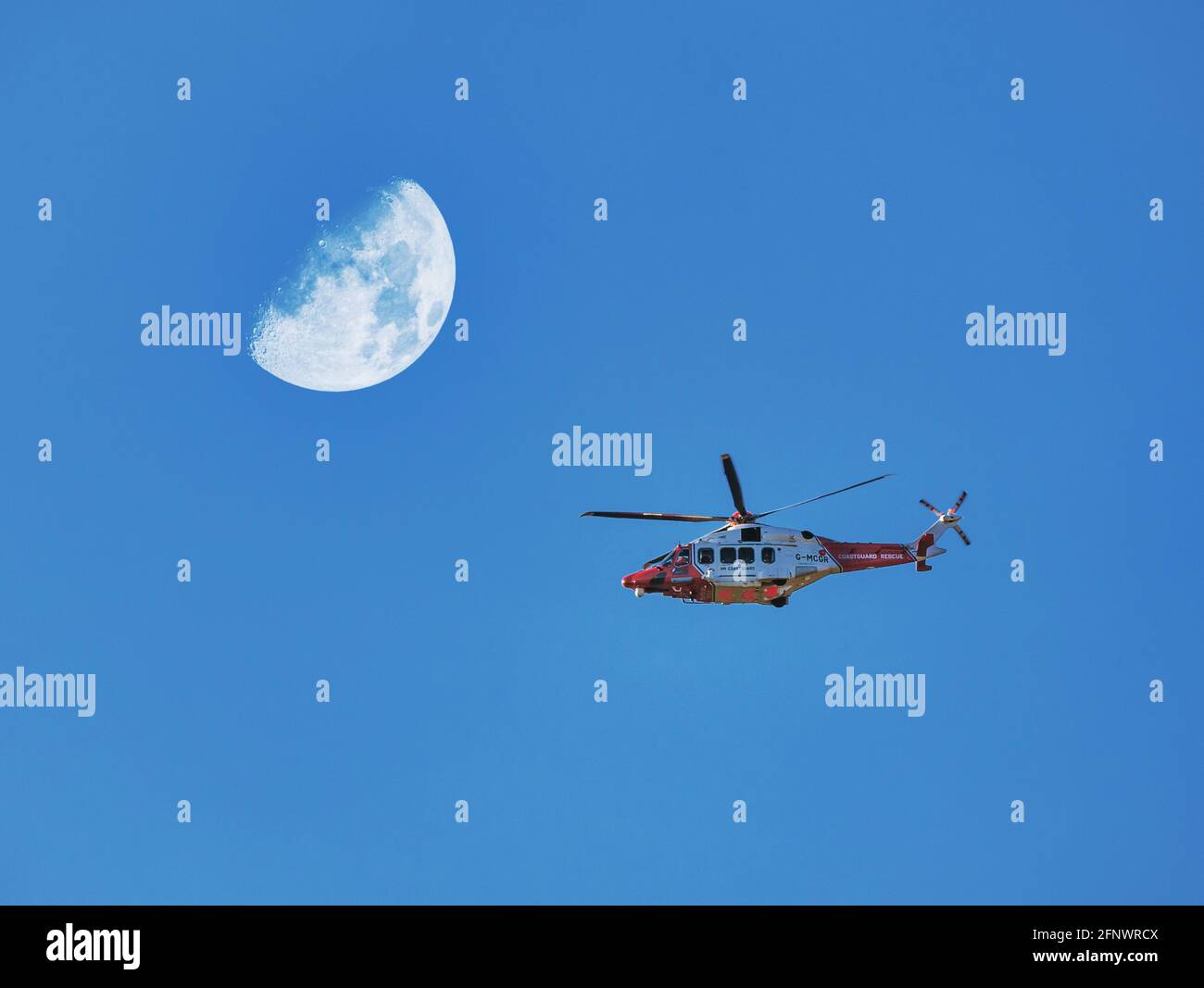 Hélicoptère de garde-côtes volant survolant un ciel bleu vif avec demi-lune, Écosse, Royaume-Uni Banque D'Images