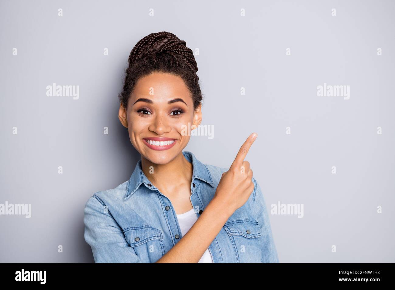 Photo portrait d'une fille avec un petit pain souriant montrant l'espace publicitaire recommandé isolé sur fond gris Banque D'Images