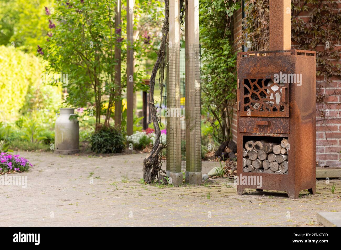 Un poêle en bois rouillé avec du bois dans un beau jardin idyllique avec des tondeuses, des arbres et de la verdure, par une journée ensoleillée, créant un paysage conscient Banque D'Images