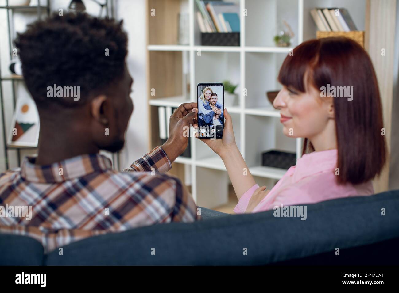 Afro-américain et caucasien ayant des appels vidéo avec des amis tout en restant à la maison. Jeune couple utilisant un smartphone moderne pour la conversation en ligne. Banque D'Images