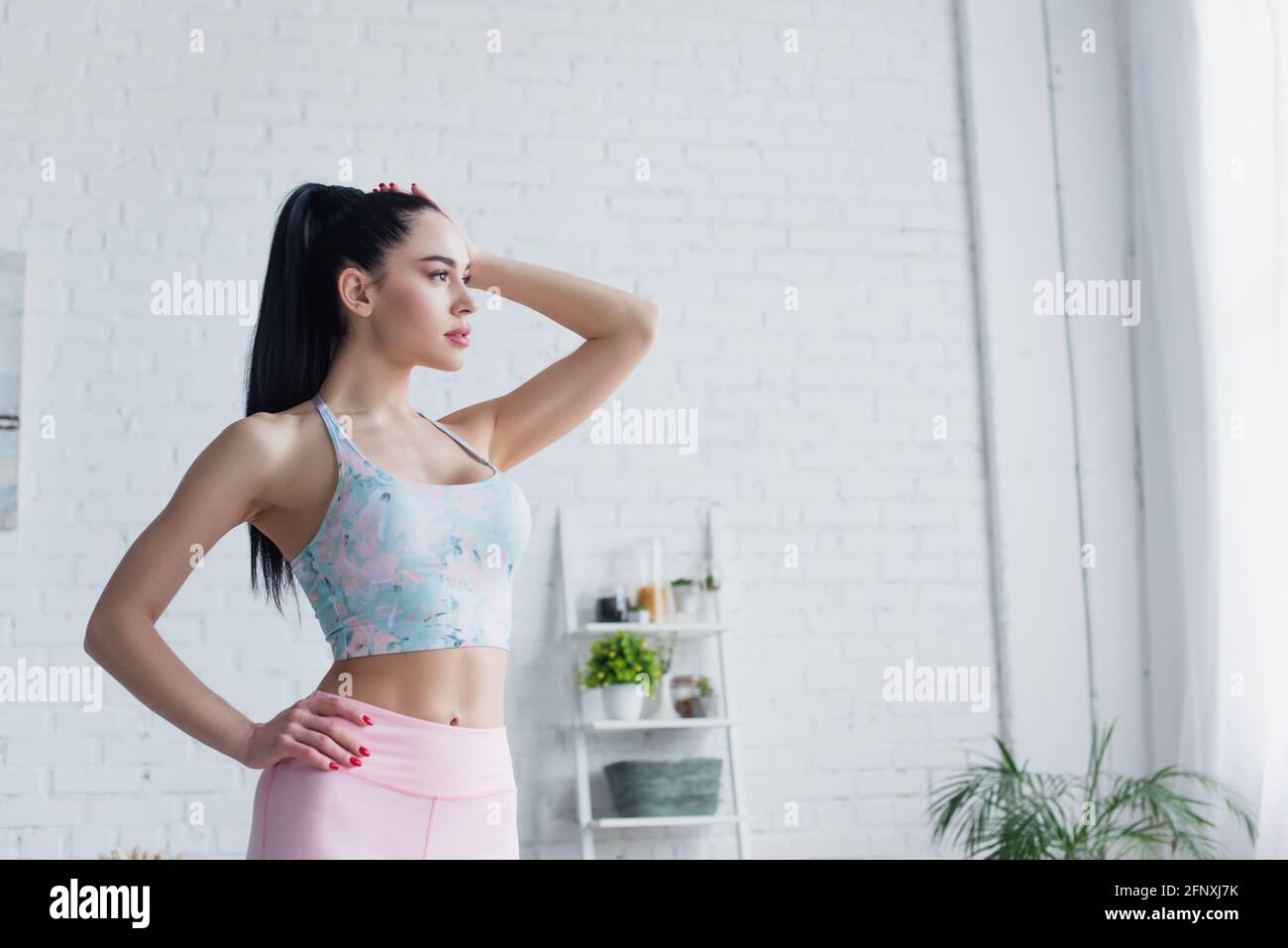 jeune sportif debout avec la main sur la hanche et regardant loin à la maison Banque D'Images