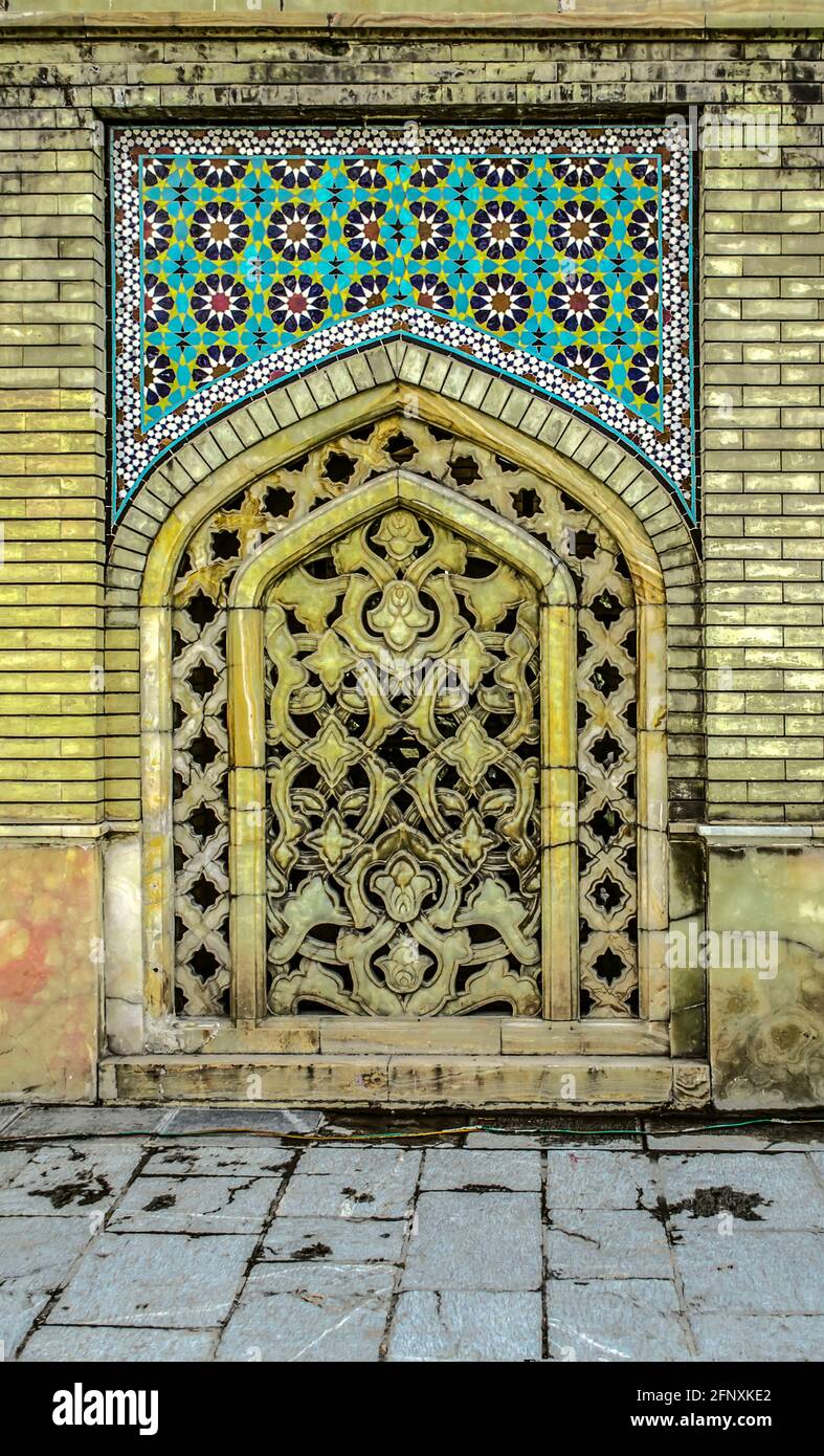 Une niche dans un mur de briques, recouvert d'un motif lumineux, avec un trou ovale recouvert d'un treillis décoratif de marbre jaune sculpté dans la Pala de Golestan Banque D'Images