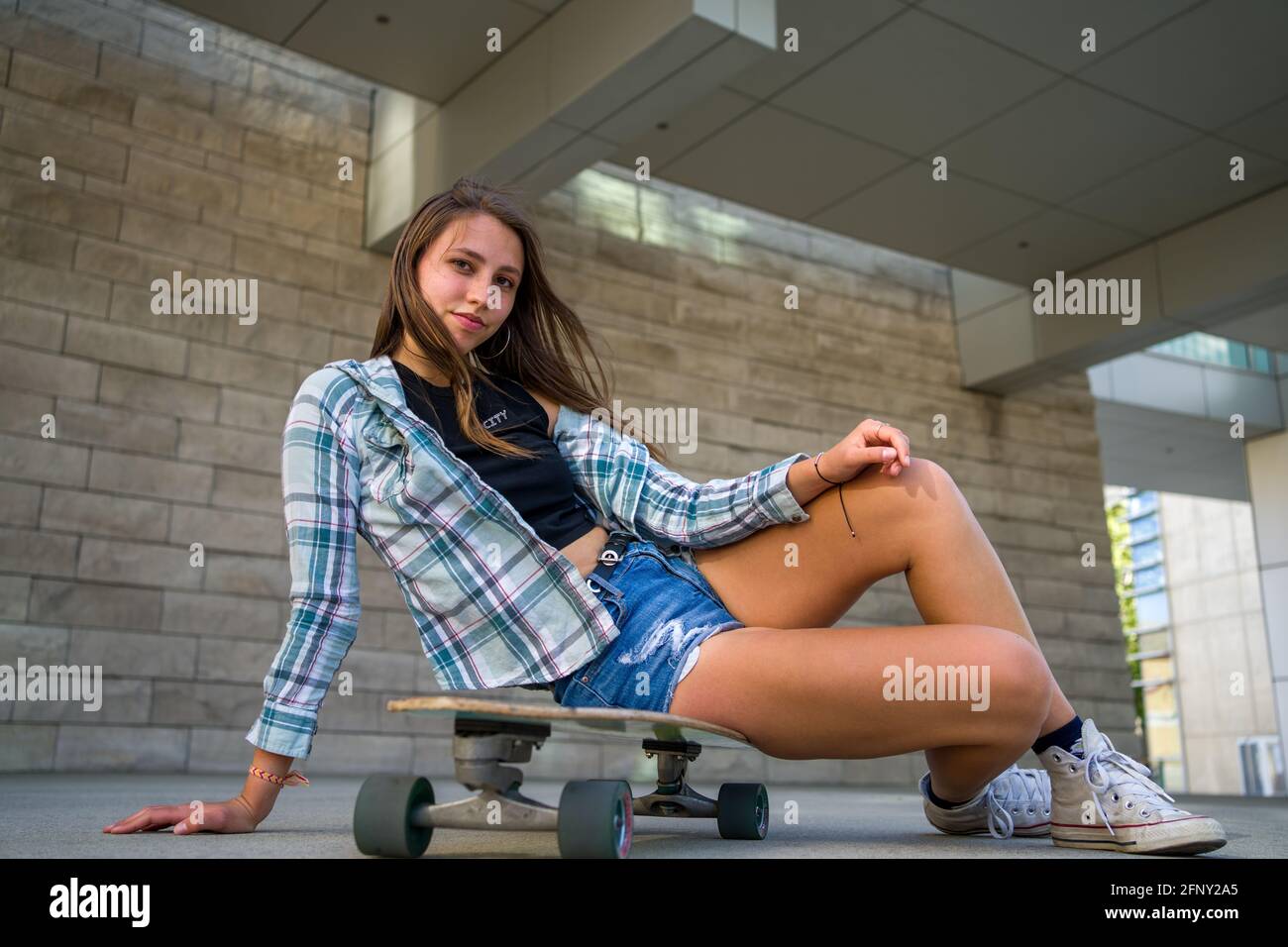 Jeune femme posant avec son skateboard dans un cadre urbain Banque D'Images