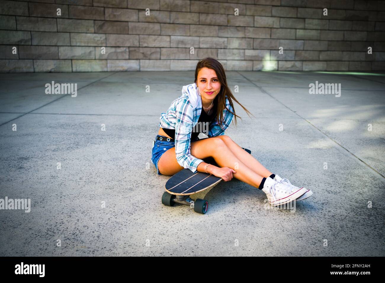 Jeune femme posant avec son skateboard dans un cadre urbain Banque D'Images