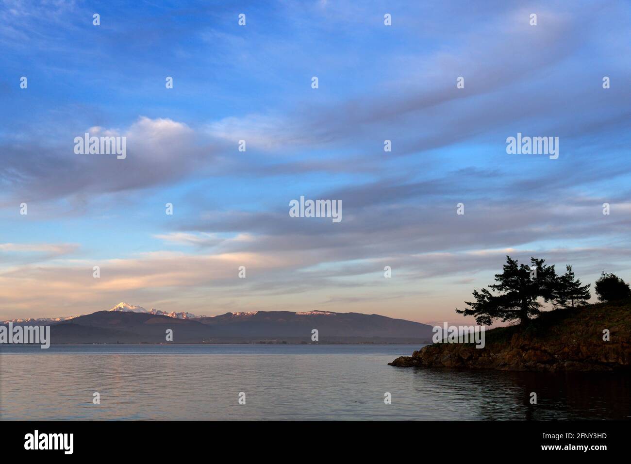 Vue sur un promontoire sur l'île de Saddlebag avec le mont Baker et les montagnes Cascade sur la baie de Padilla en arrière-plan pendant le coucher du soleil, Saddlebag Island Marine Banque D'Images