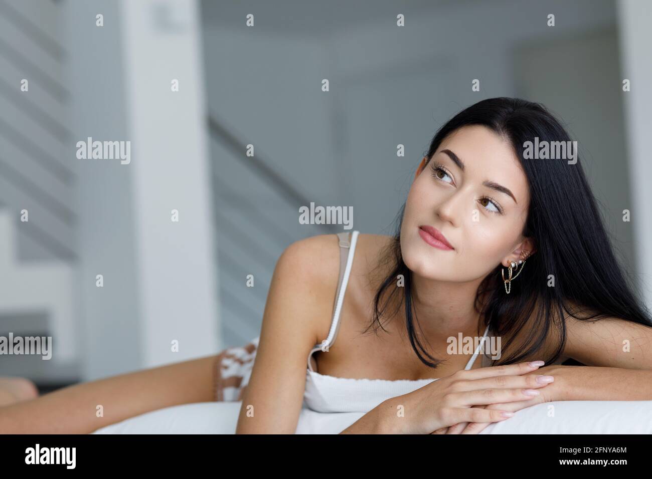 Une jeune femme qui ment du jour rêvant ou qui pense à ses aspirations mensongeuses détente sur un canapé en vêtements de loisirs en regardant sur le côté avec une expression lointaine Banque D'Images