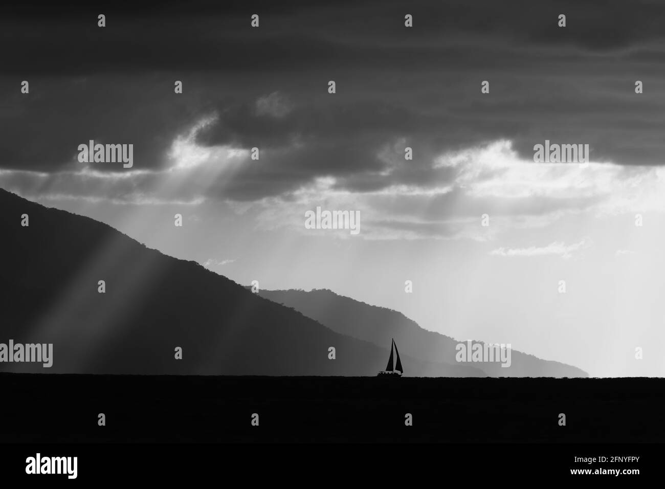 Un Voilier est silhoueté contre les rayons du soleil qui s'envolent L'horizon océanique au format d'image noir et blanc Banque D'Images