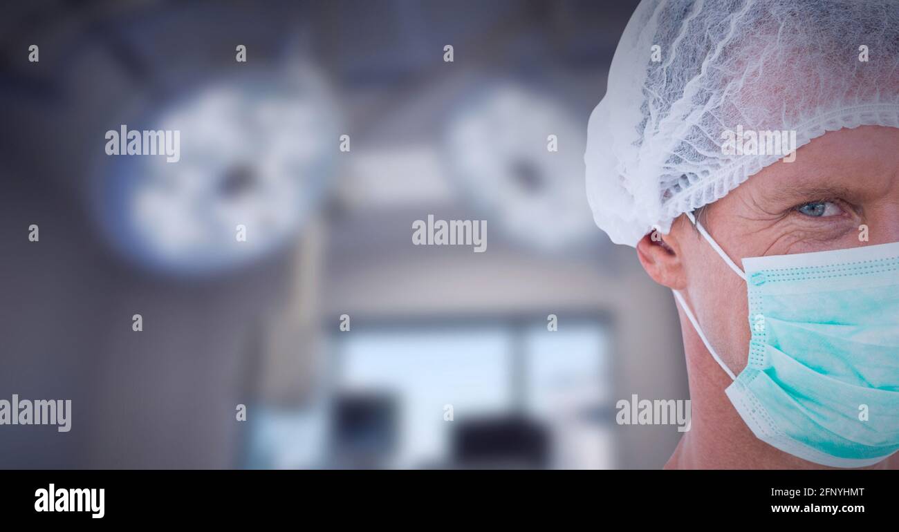 Portrait court d'un chirurgien mâle caucasien portant un masque facial contre lumières chirurgicales en arrière-plan Banque D'Images
