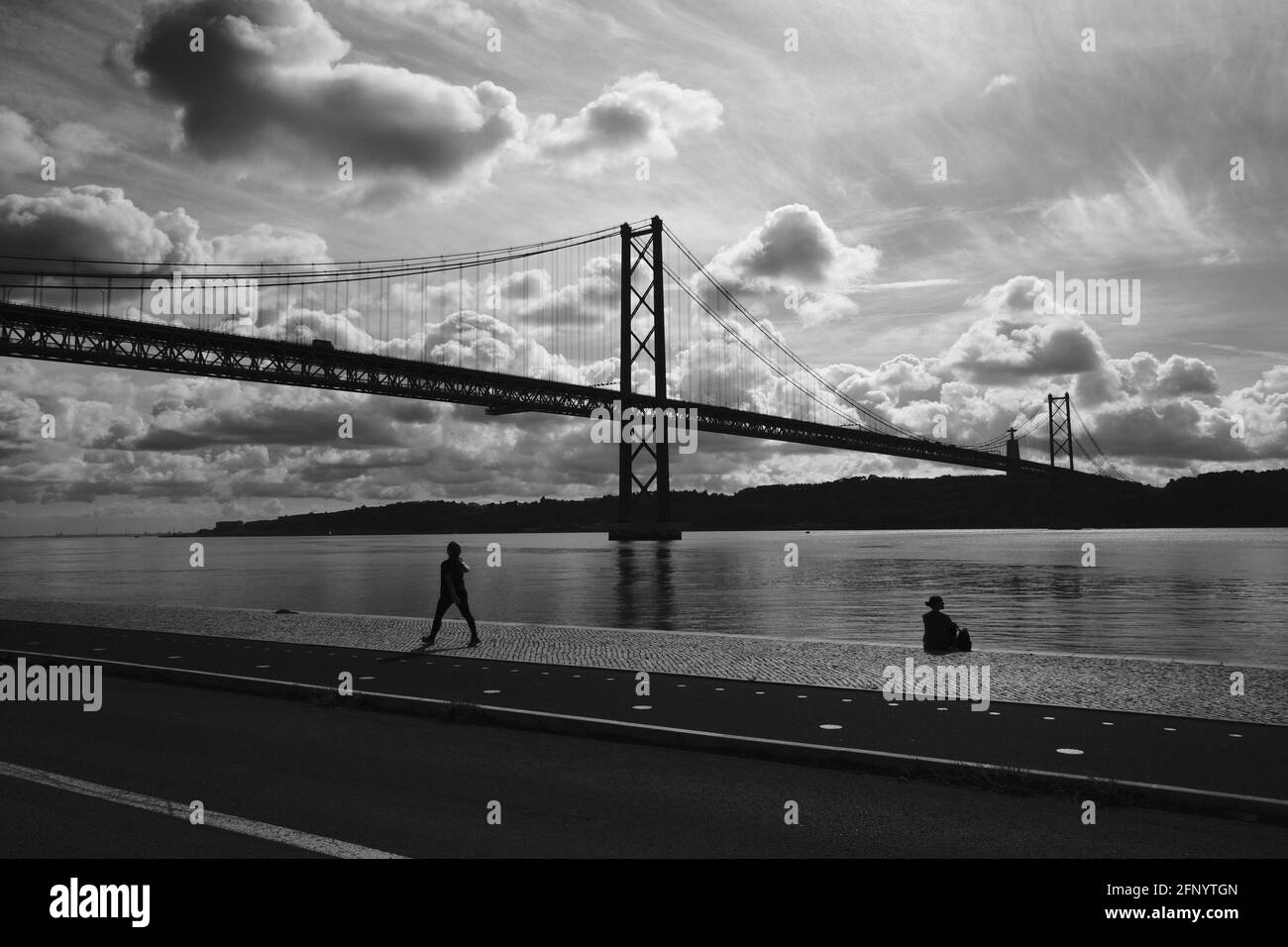 Silhouette de deux personnes se détendant au bord de la rivière sous un ciel nuageux et ensoleillé à Lisbonne, Portugal. Banque D'Images