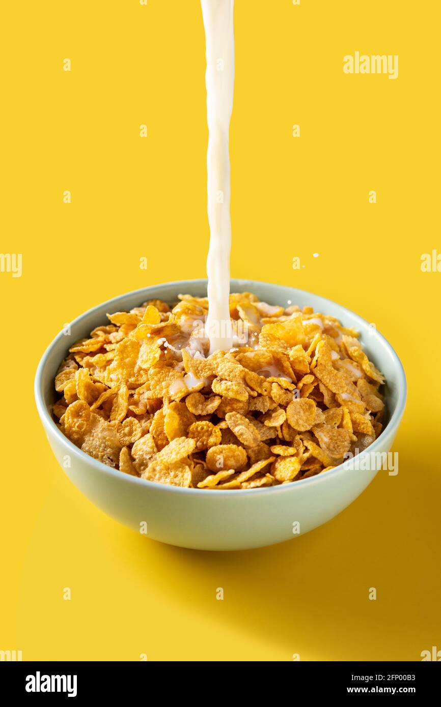 Verser le lait dans un bol de flocons de maïs sur fond jaune Banque D'Images