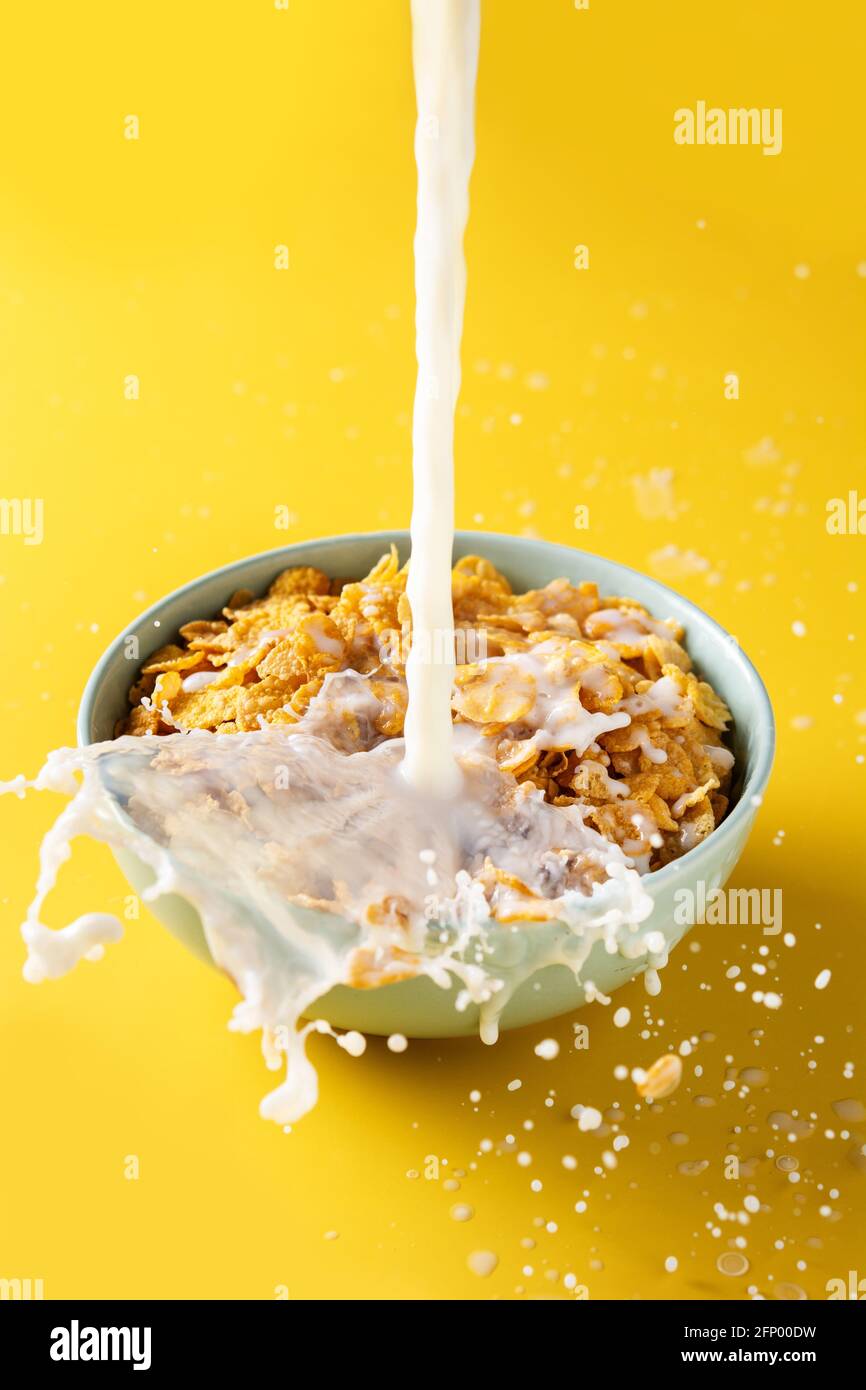 Verser le lait dans un bol de flocons de maïs sur fond jaune Banque D'Images