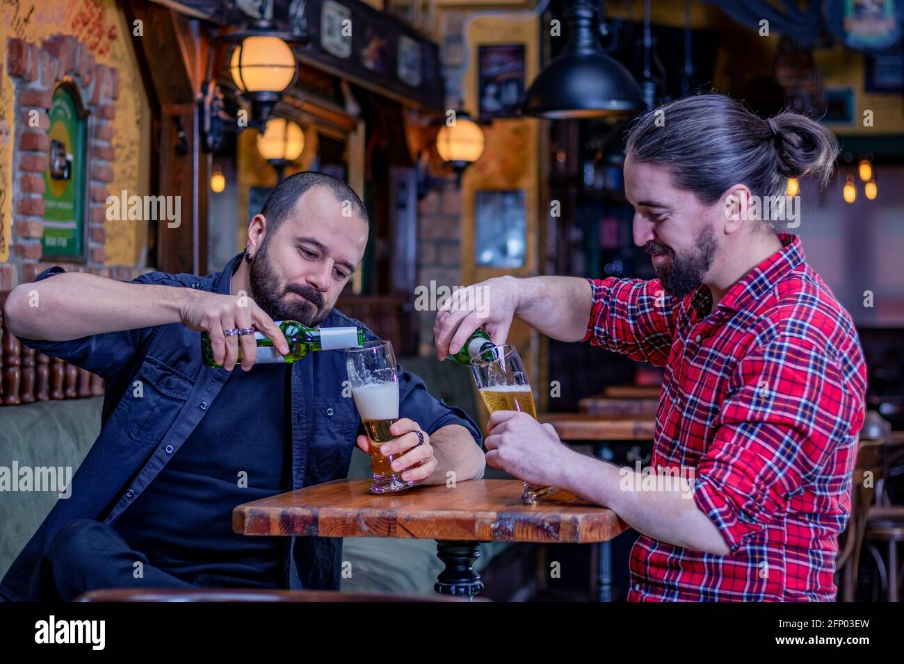 Deux amis de sexe masculin buvant au pub. Verser la bière de la bouteille dans de grands verres. Retour à la vie normale. Banque D'Images