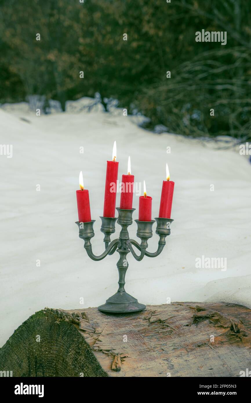 bougie étain avec cinq bougies rouges sur un tronc d'arbre extérieur en hiver Banque D'Images