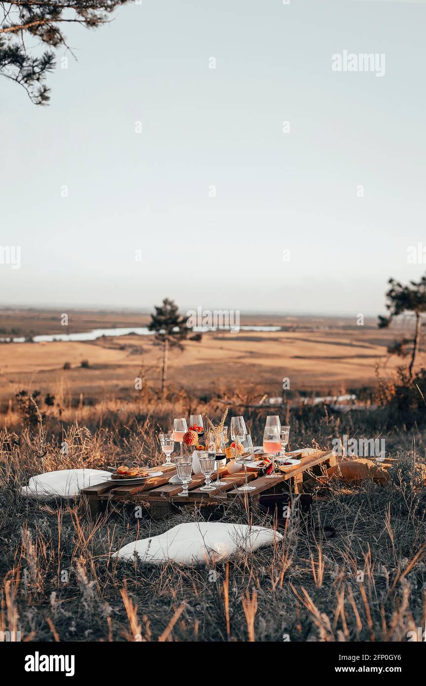 Ensemble de verres élégants placés sur une table en bois de planche avec arrangement floral sur prairie herbacée pendant pique-nique d'automne festif Banque D'Images