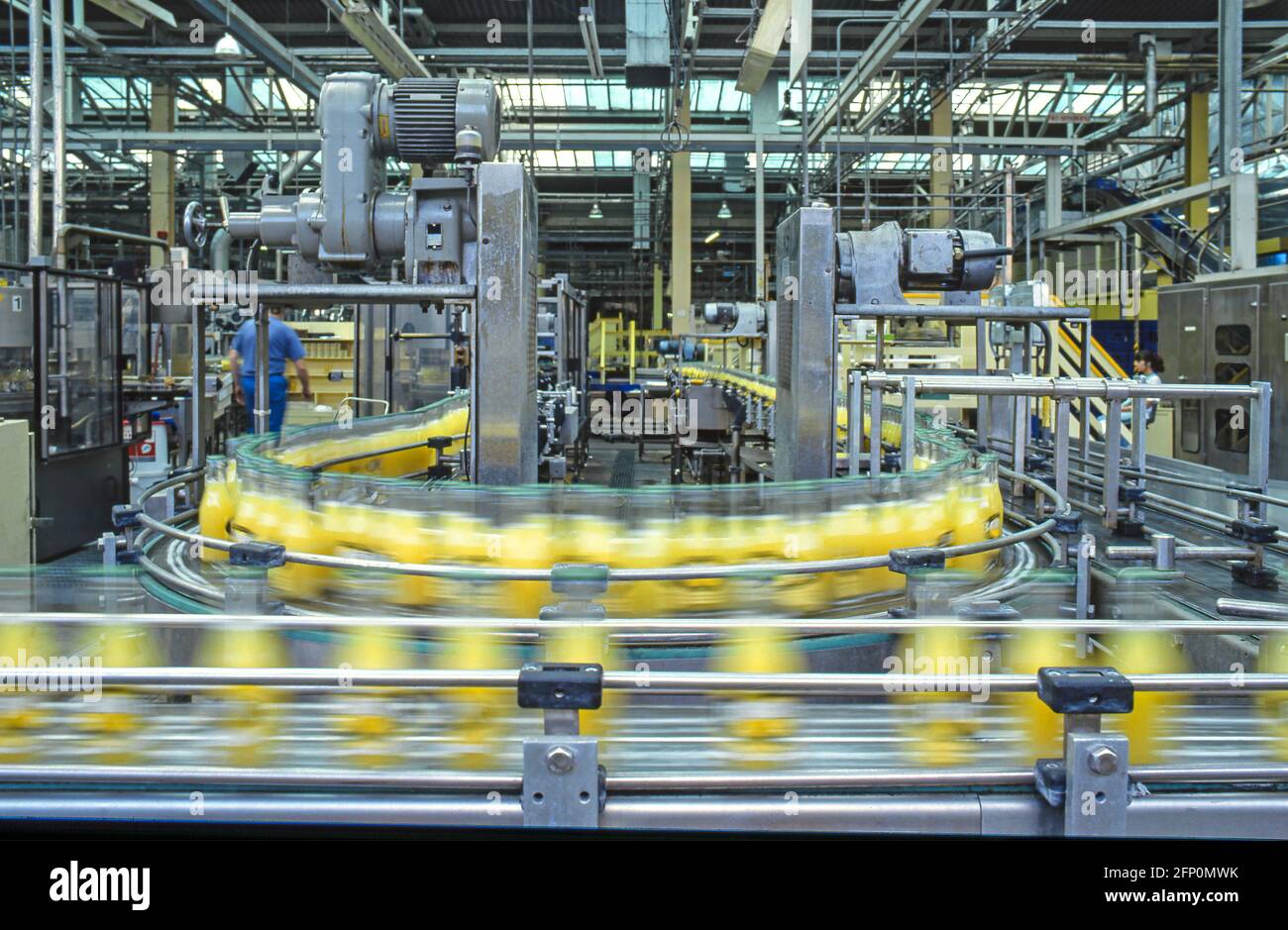 Machines fonctionnant avec un tapis transporteur de type chaîne d'assemblage de production de masse automatisée les bouteilles en verre à boisson douce sont floues à l'intérieur de l'usine Angleterre Royaume-Uni Banque D'Images