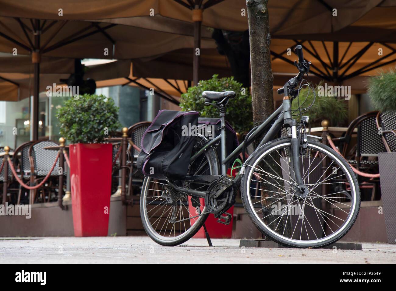Vélo noir avec sac à valises doubles garé sous l'arbre près de la terrasse du café Banque D'Images