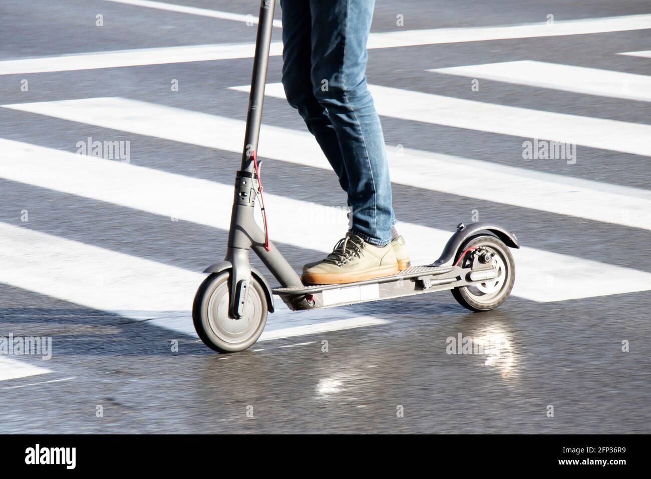 Belgrade, Serbie - 13 mai 2021 : gros plan de jambes de personnes à bord d'un scooter électrique en traversant la rue humide par un beau jour ensoleillé et pluvieux Banque D'Images