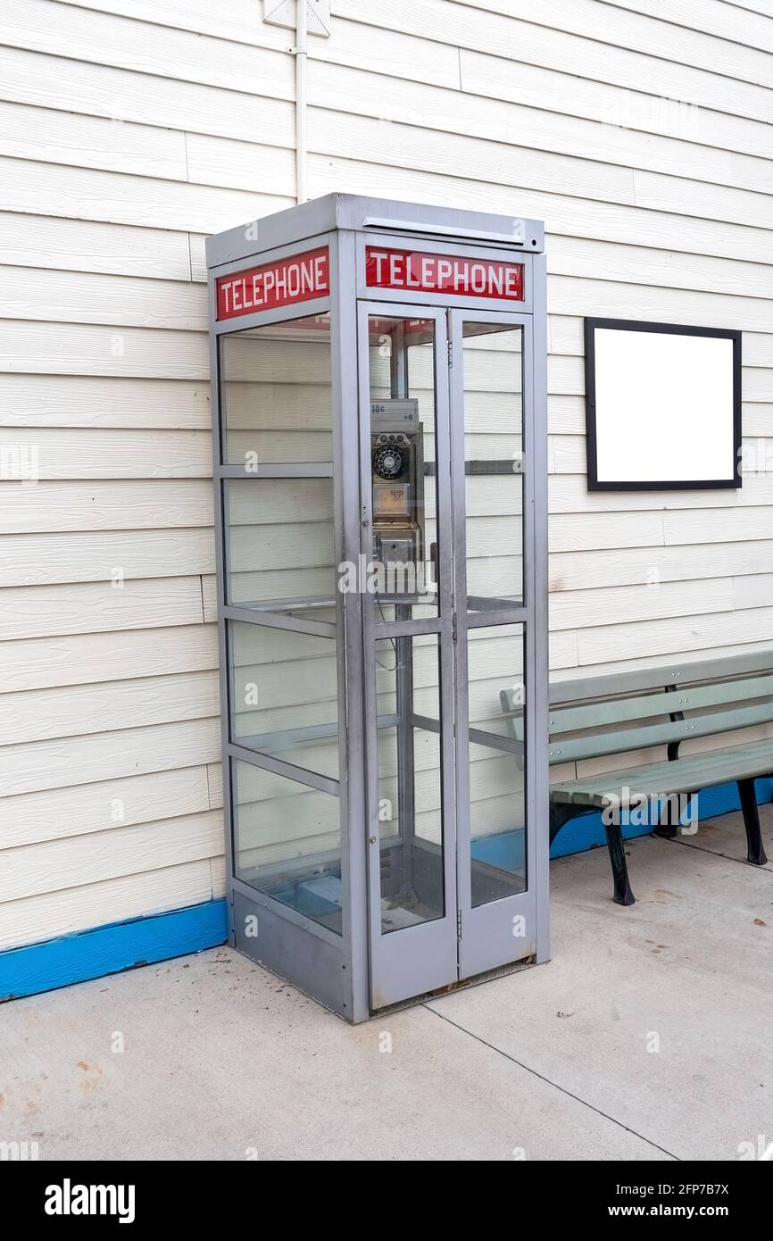Photo verticale d'une ancienne cabine téléphonique avec un panneau vierge sur le mur à côté de celui-ci, sur le côté droit. Il y a un banc sous l'affiche. Banque D'Images