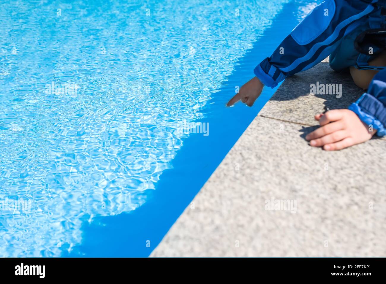 La main d'un enfant touche l'eau bleue dans la piscine, la piscine et le pont de mramor idéal pour les arrière-plans, les vacances d'été Banque D'Images