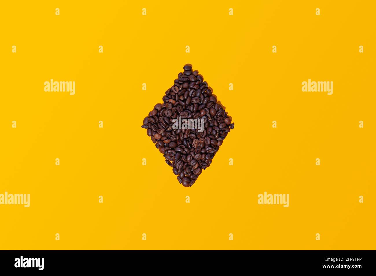 Grains de café regroupés formant la figure d'un diamant de carte à jouer isolé sur un fond jaune vu d'en haut. Il y a de l'espace pour le texte Banque D'Images