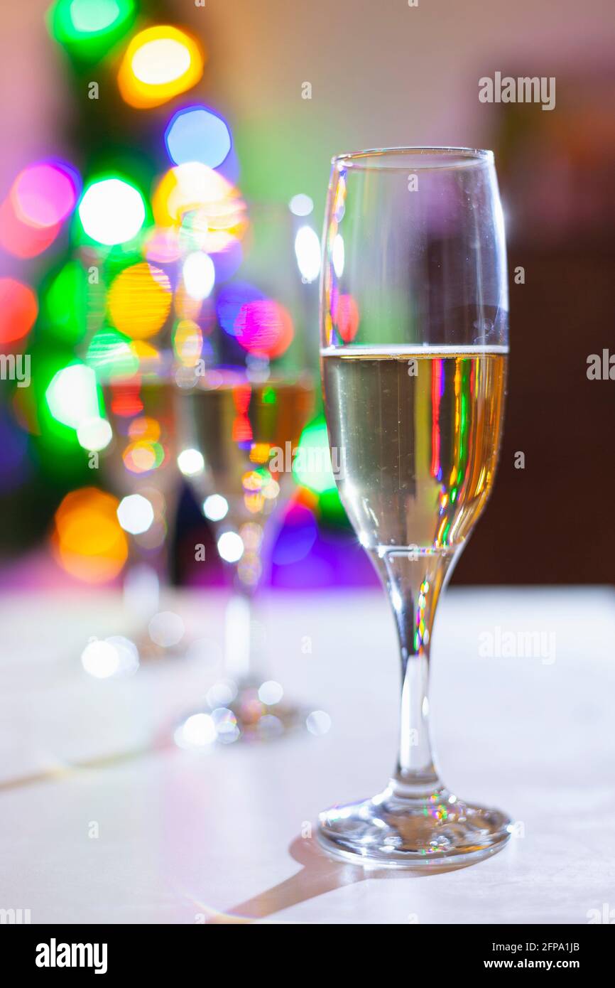 Trois verres de champagne sur une table blanche, la première est en vue. En arrière-plan, les lumières colorées d'un arbre de Noël sont hors foyer. Une intention Banque D'Images