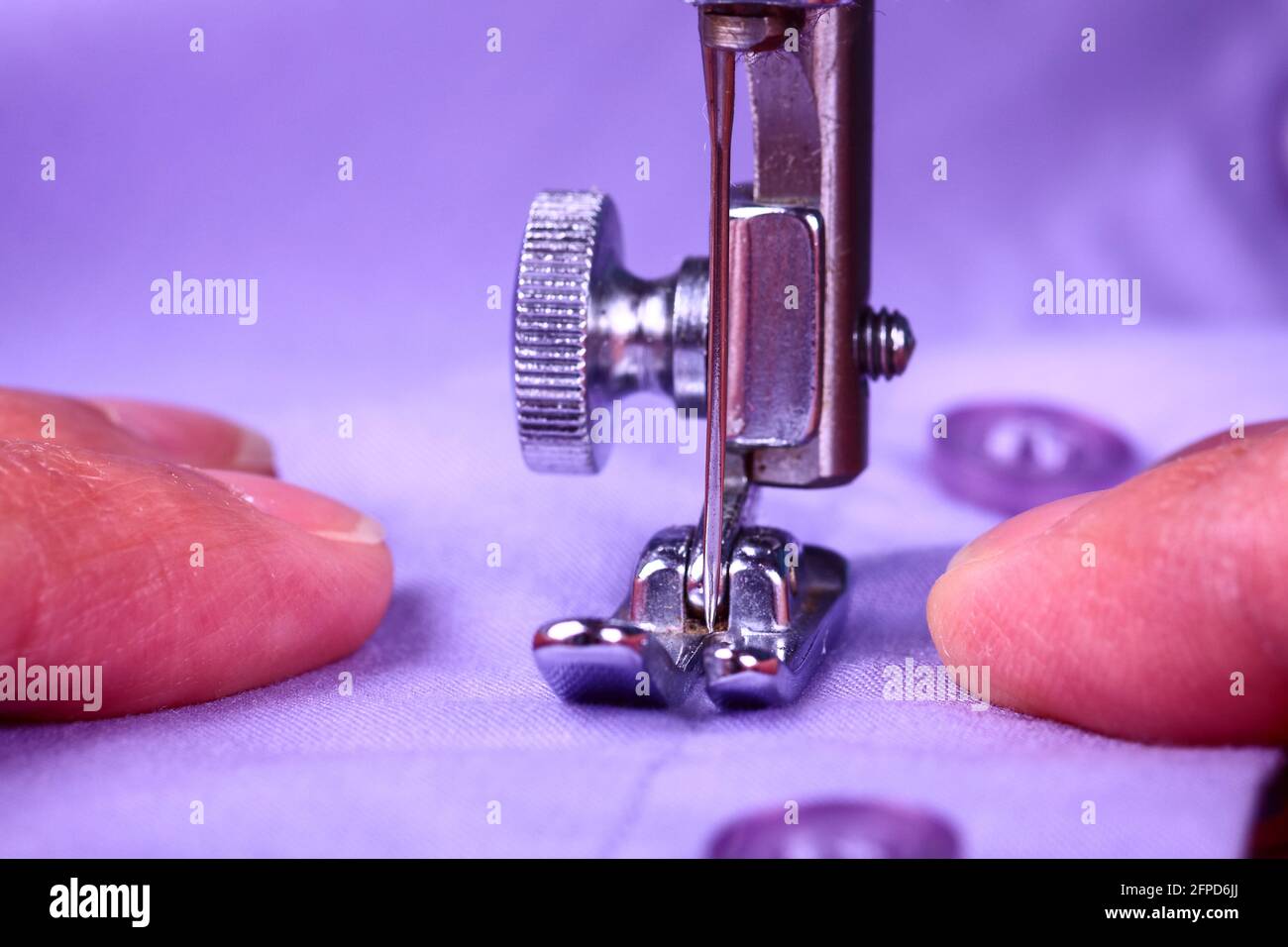 Les mains d'une femme guidant une chemise de couleur lilas à travers un vintage machine à coudre Banque D'Images