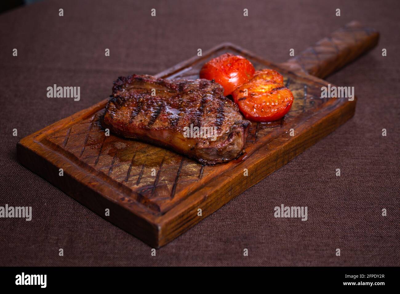 délicieux steak sur un os avec des tomates sur une planche de bois. Banque D'Images