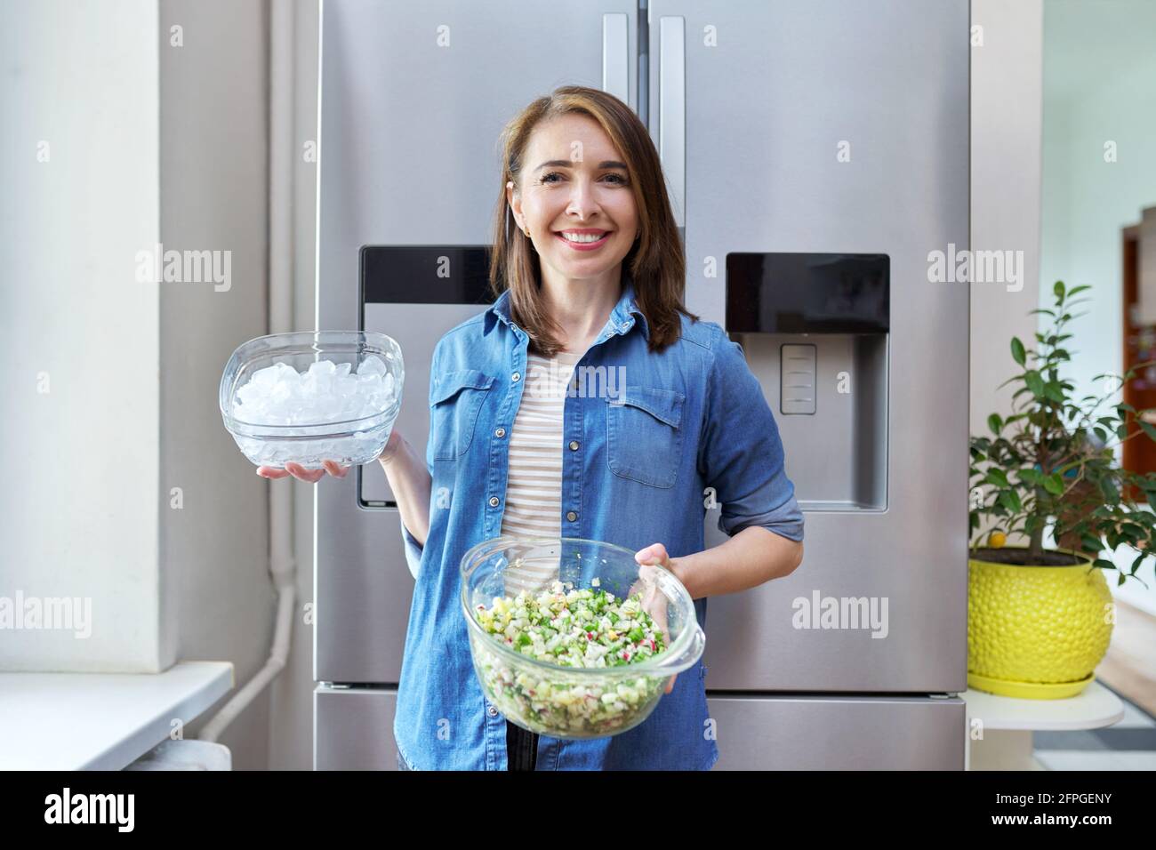 Femme souriante avec un bol de glace et une assiette de légumes salade dans ses mains Banque D'Images