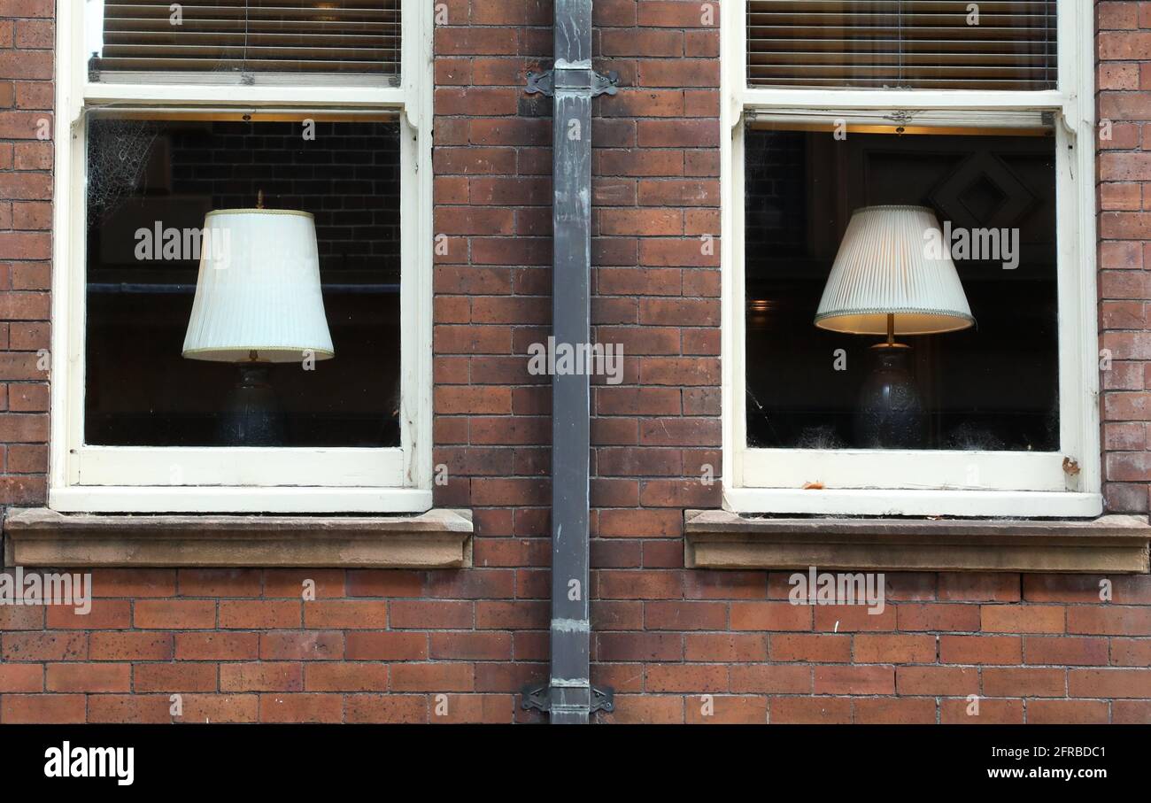 deux appartements en brique intérieure ou des bureaux avec des cadres de fenêtre identiques divisé au milieu par un tuyau en bas. Deux abat-jour similaires dans la fenêtre. Banque D'Images