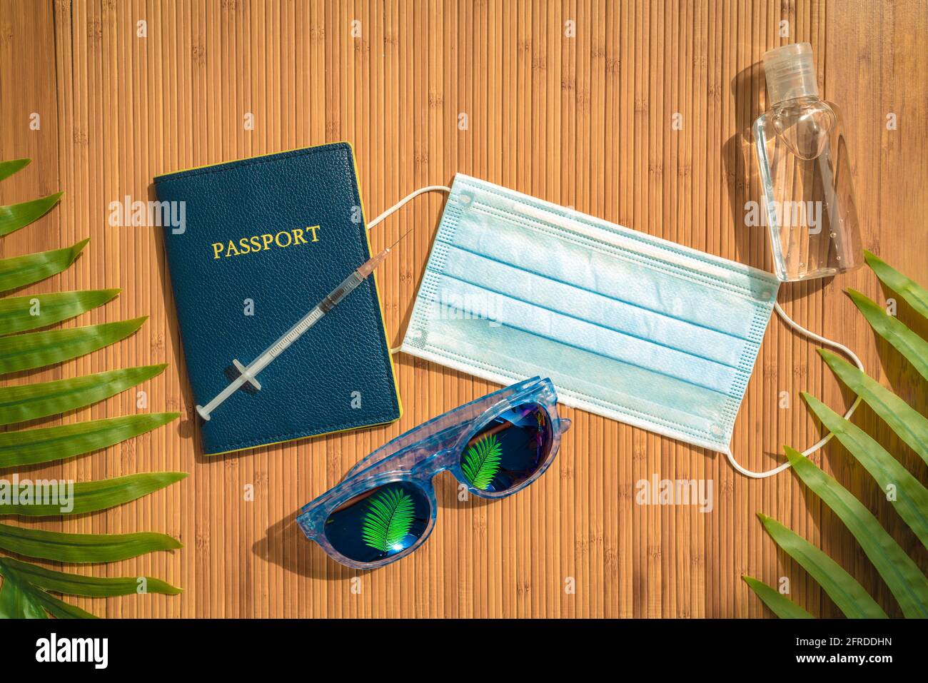Passeport pour les vacances d'été. Masque facial, bouteille d'assainisseur pour les mains, lunettes de soleil, articles essentiels pour les fêtes. Vue de dessus sur fond en bambou Banque D'Images