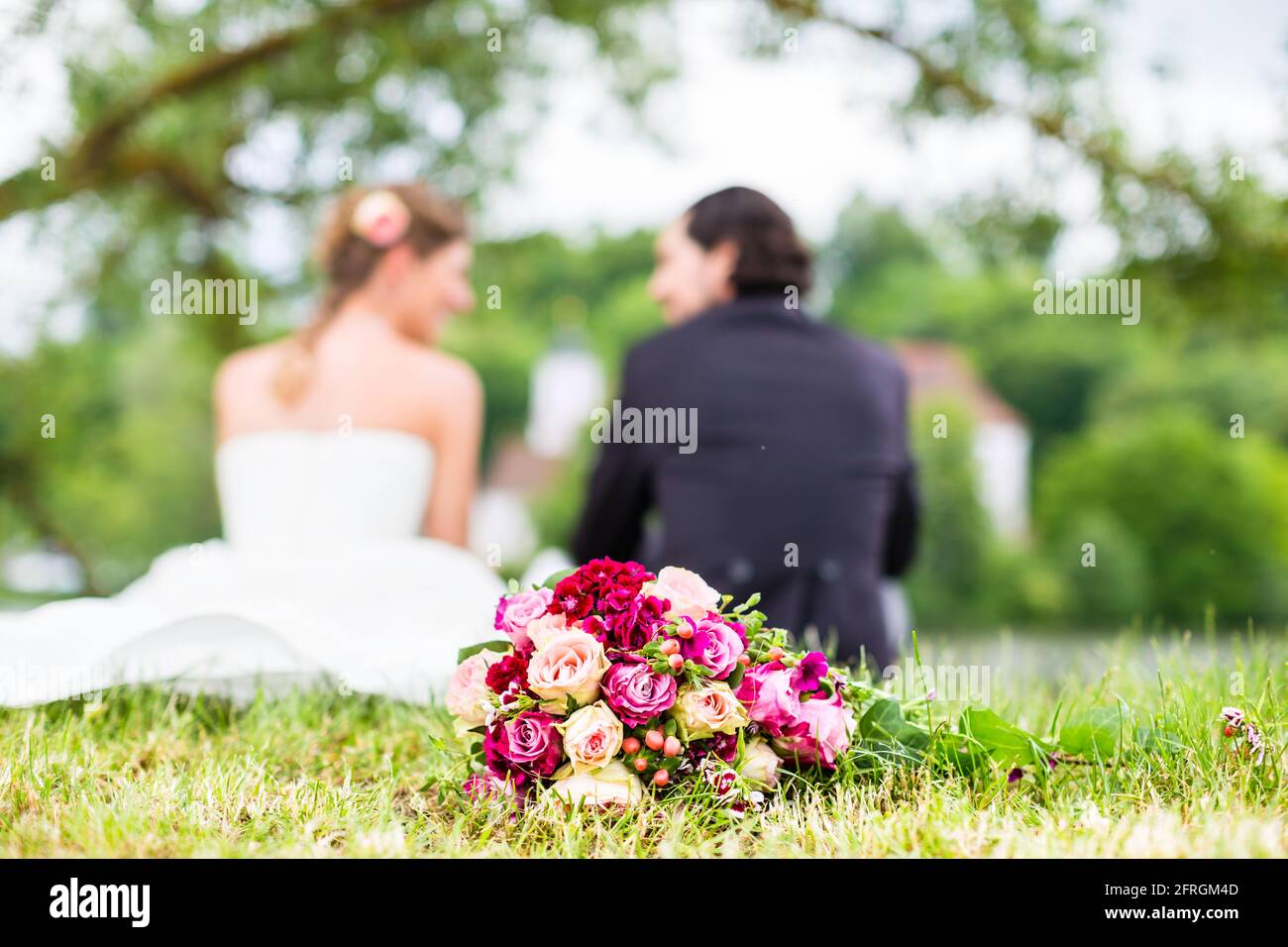 Couple de mariés assis sur la prairie avec bouquet de mariée derrière eux, francs shot Banque D'Images