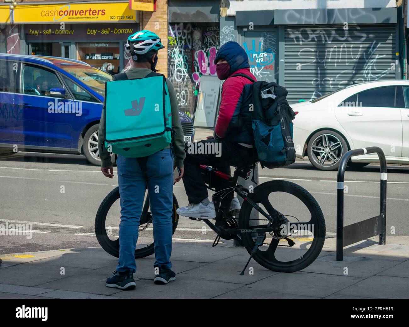 Londres. Royaume-Uni- 05.18.2021: Deux jeunes hommes travaillant en tant que travailleurs indépendants de livraison à domicile riders travaillant pour les compagnies de commande de nourriture en ligne ayant un chat. Banque D'Images