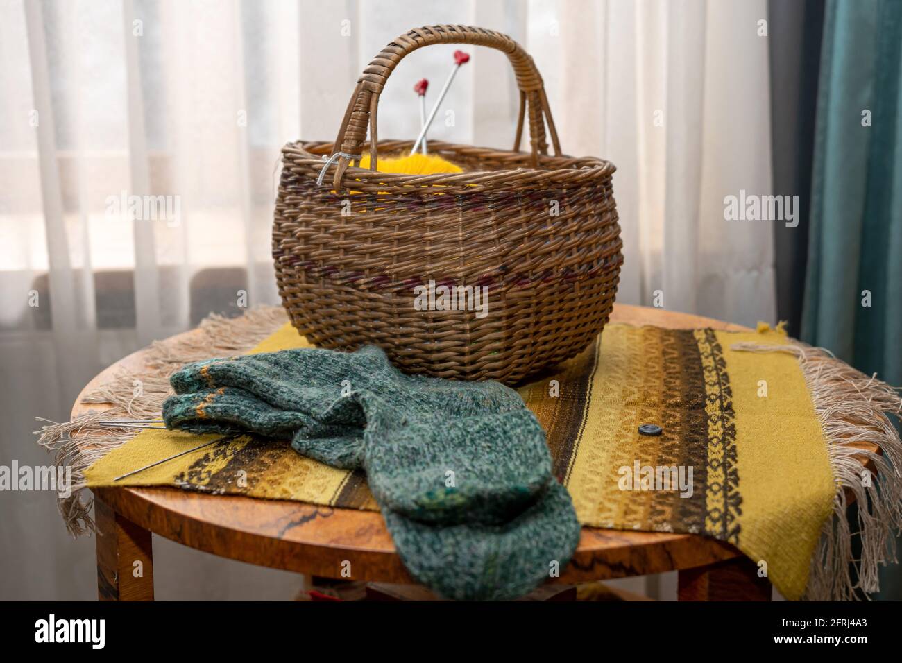 Intérieur vintage, chaussettes tricotées et panier en osier avec fil sur une table ronde en bois recouverte d'une couverture populaire, gros plan Banque D'Images