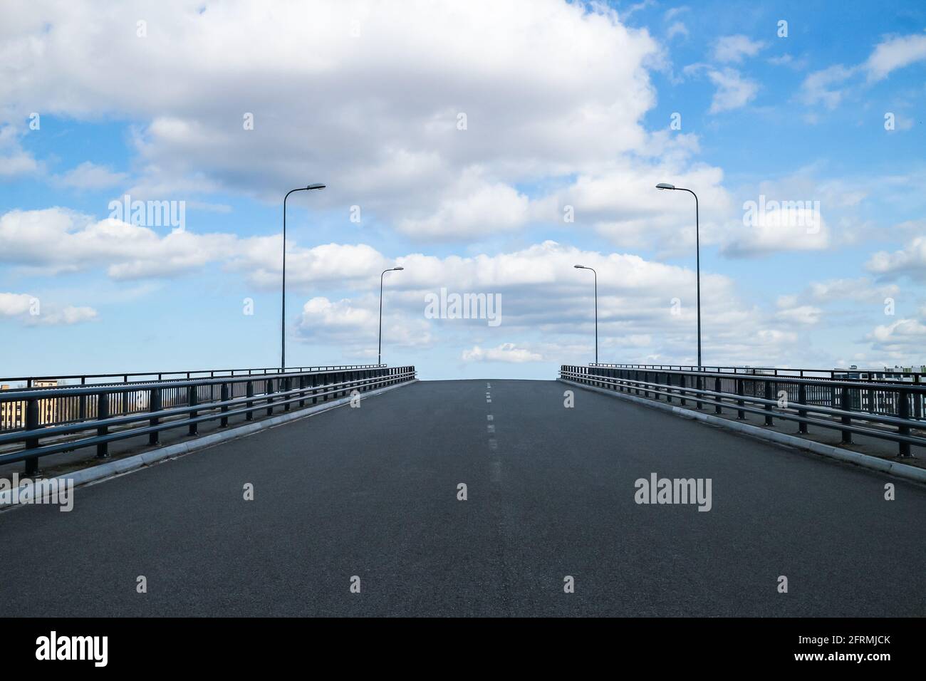 Route asphaltée avec une clôture de sécurité pour piétons contre un ciel bleu avec des nuages. Infrastructure urbaine, construction et entretien de routes. Banque D'Images