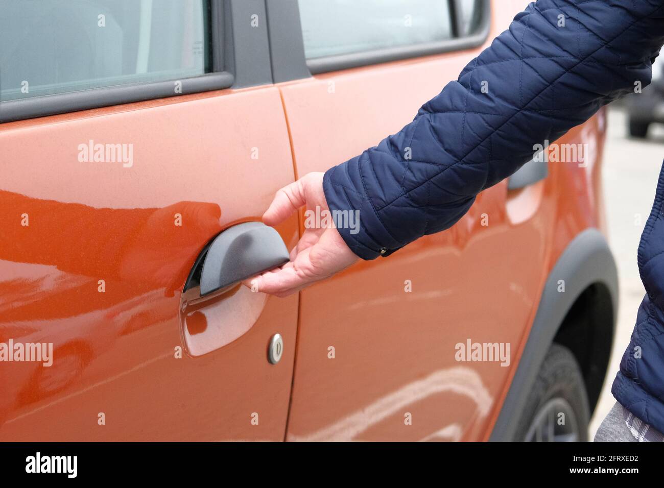 L'homme ouvre la porte de sa voiture orange dans le parking. Main sur la poignée. Gros plan. Banque D'Images