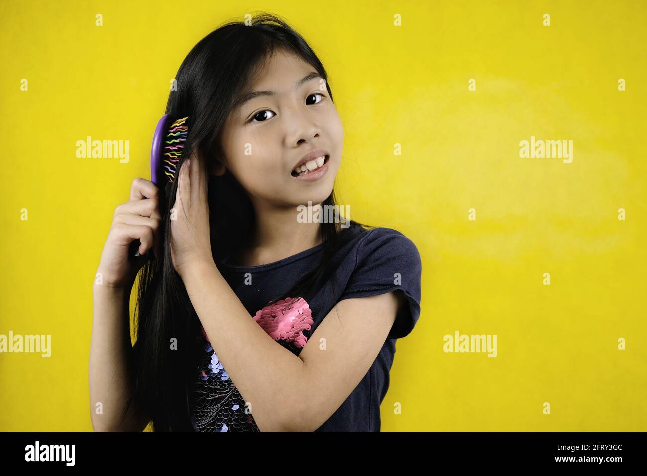 Une jeune fille asiatique mignonne ses beaux cheveux longs et foncés à l'aide d'un peigne après la douche, se sentent détendus et heureux, souriant. Arrière-plan jaune vif Banque D'Images
