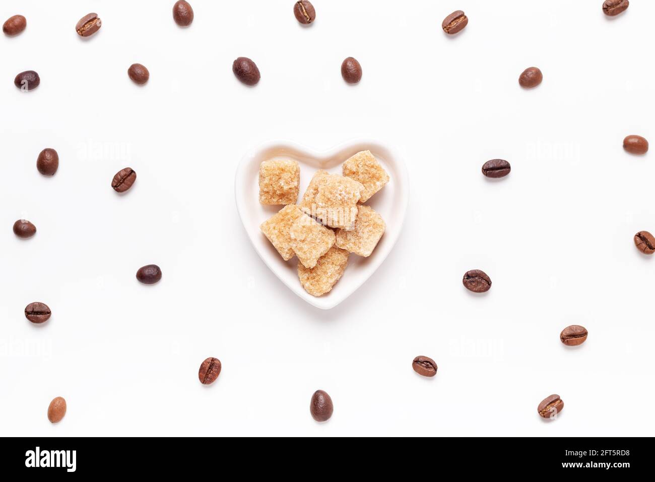 Faire dorer les morceaux de sucre dans une assiette en forme de cœur et les grains de café torréfiés sur fond blanc. Vue de dessus. Espace de copie - image Banque D'Images