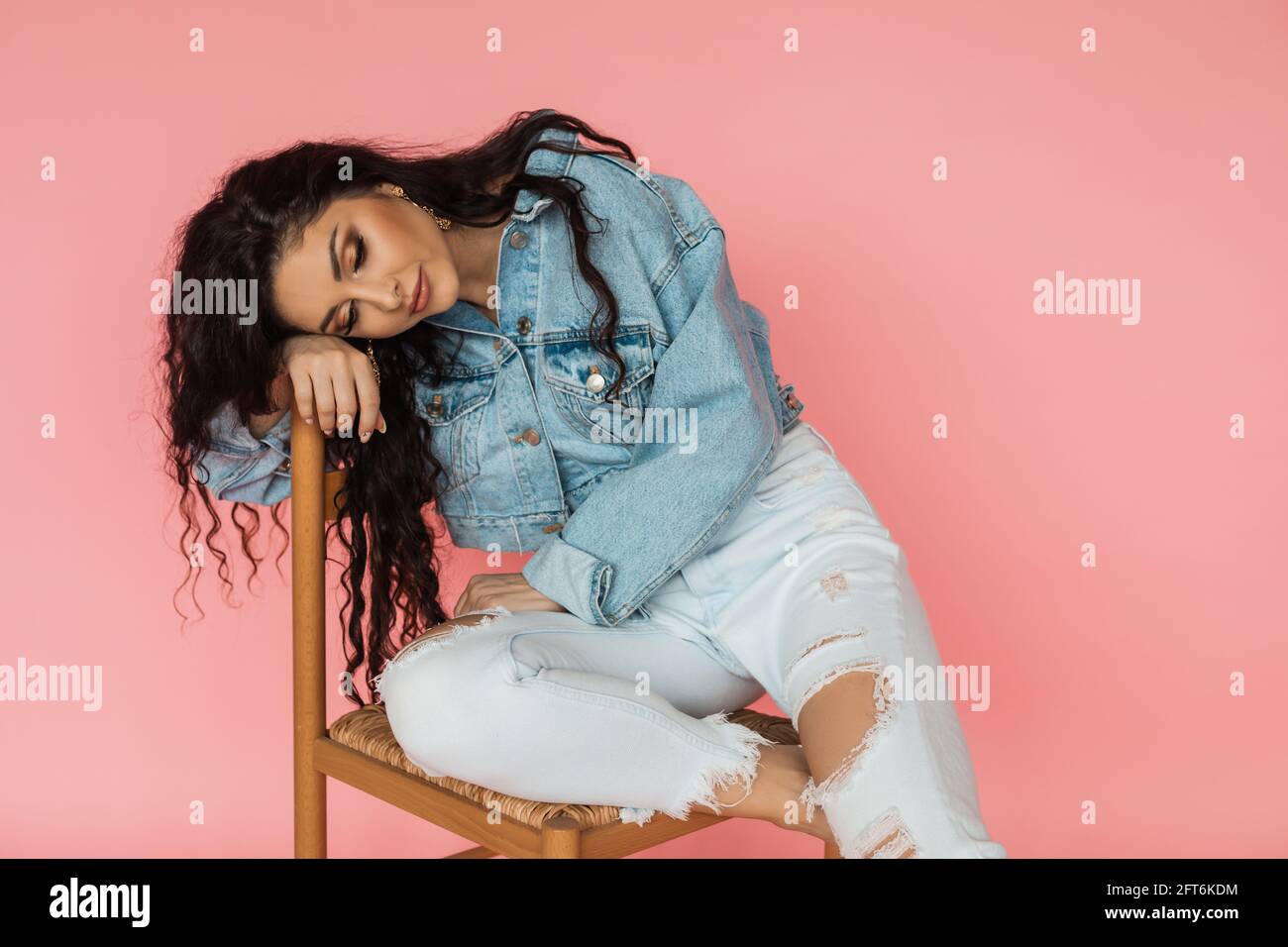 Problèmes émotionnels et psychologiques. Une fille triste et déçue est assise sur une chaise en veste denim sur fond rose Banque D'Images