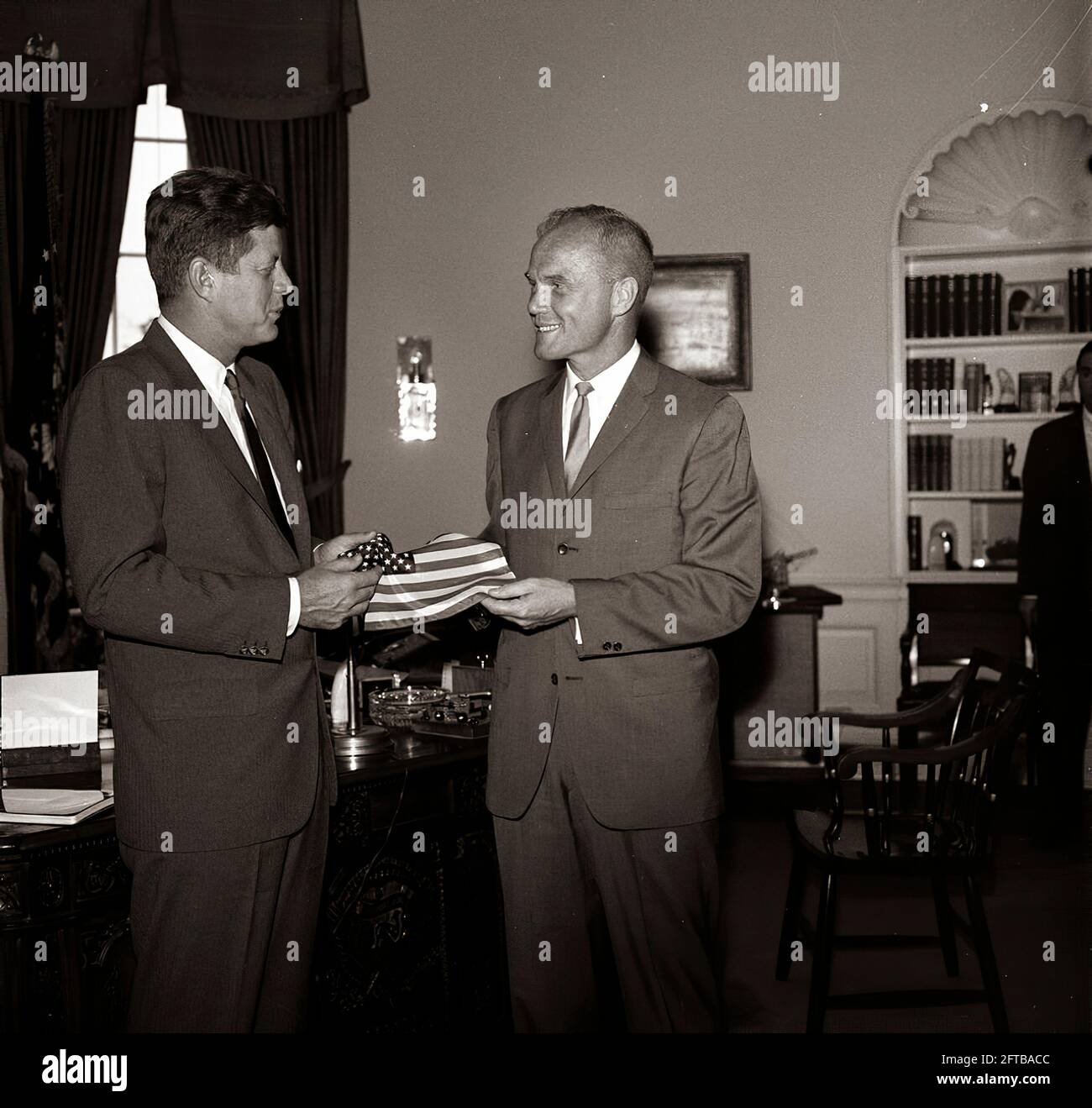 Le président John F. Kennedy reçoit un drapeau américain du lieutenant-colonel John H. Glenn Jr. (À droite) de l'astronaute; le lieutenant-colonel Glenn a porté le drapeau dans sa combinaison spatiale lors de son vol orbital à bord de Mercury-Atlas 6, également connu sous le nom d'Friendship 7. L'assistant spécial du Président, Kenneth P. O'Donnell, est en arrière-plan. Oval Office, Maison Blanche, Washington, D.C. Banque D'Images