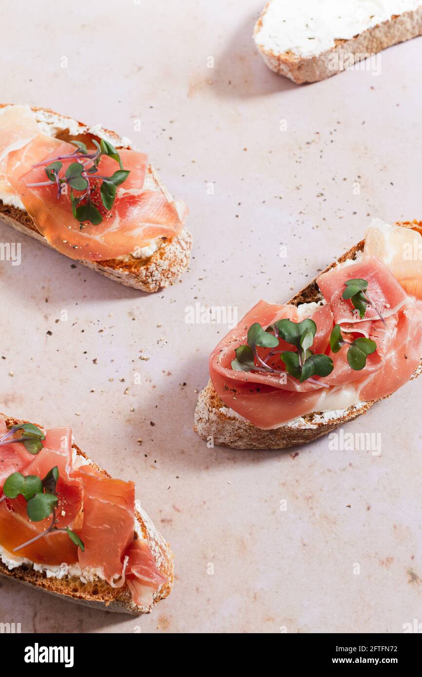 Tranches de baguette recouvertes de fromage à la crème fouettée, de jambon Serrano et de micro herbes. Banque D'Images