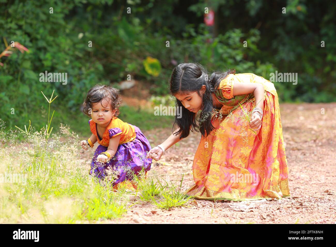 Fille indienne du Sud enfants portant belle robe traditionnelle jupe longue et chemisier, pleurs les fleurs de l'herbe de cheveux ondulée, fond de verdure. Banque D'Images