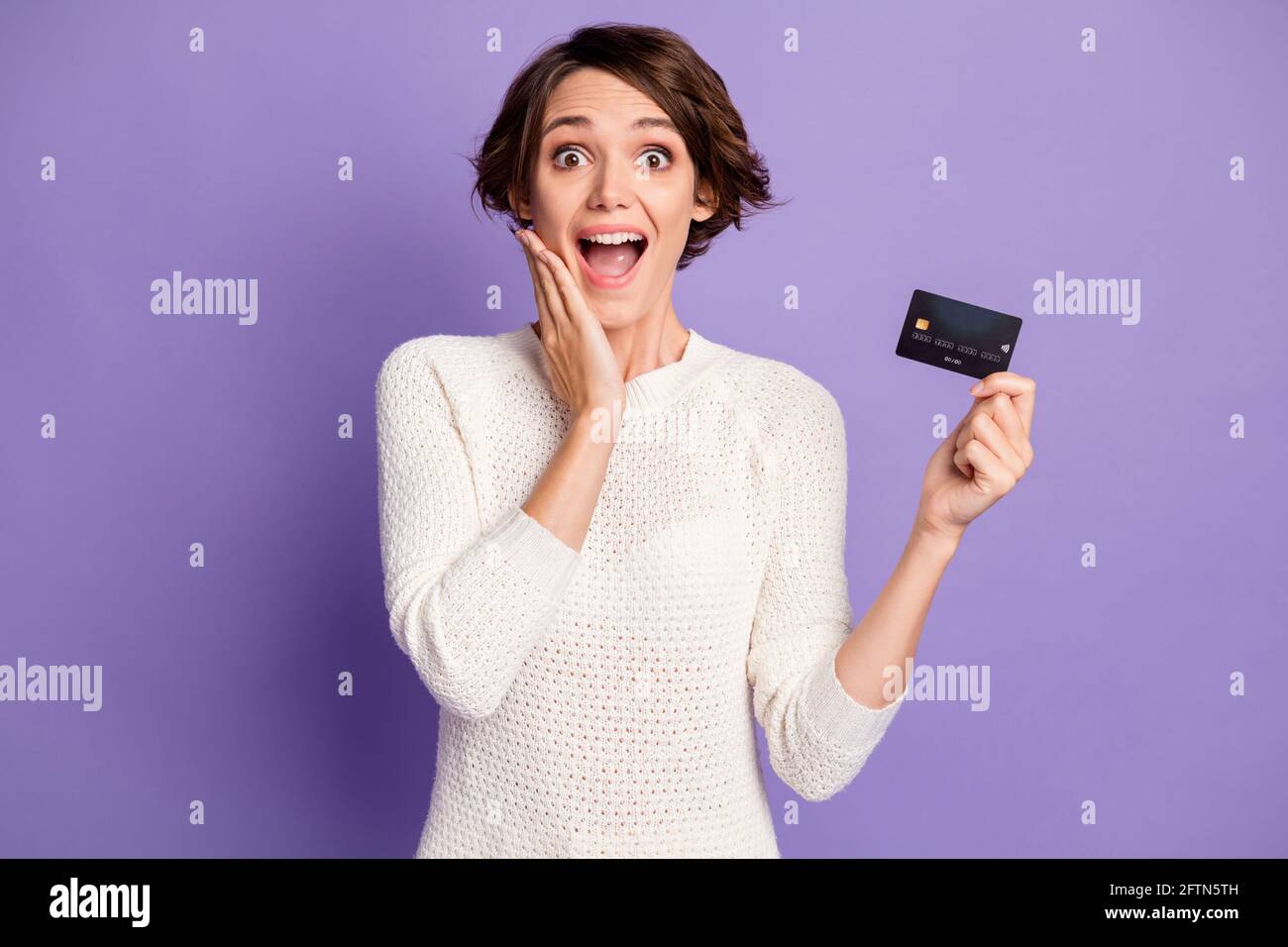 Photo portrait d'une fille gaie choquée avec carte de débit en plastique joue touchante ouverte bouche isolée sur fond violet vif Banque D'Images