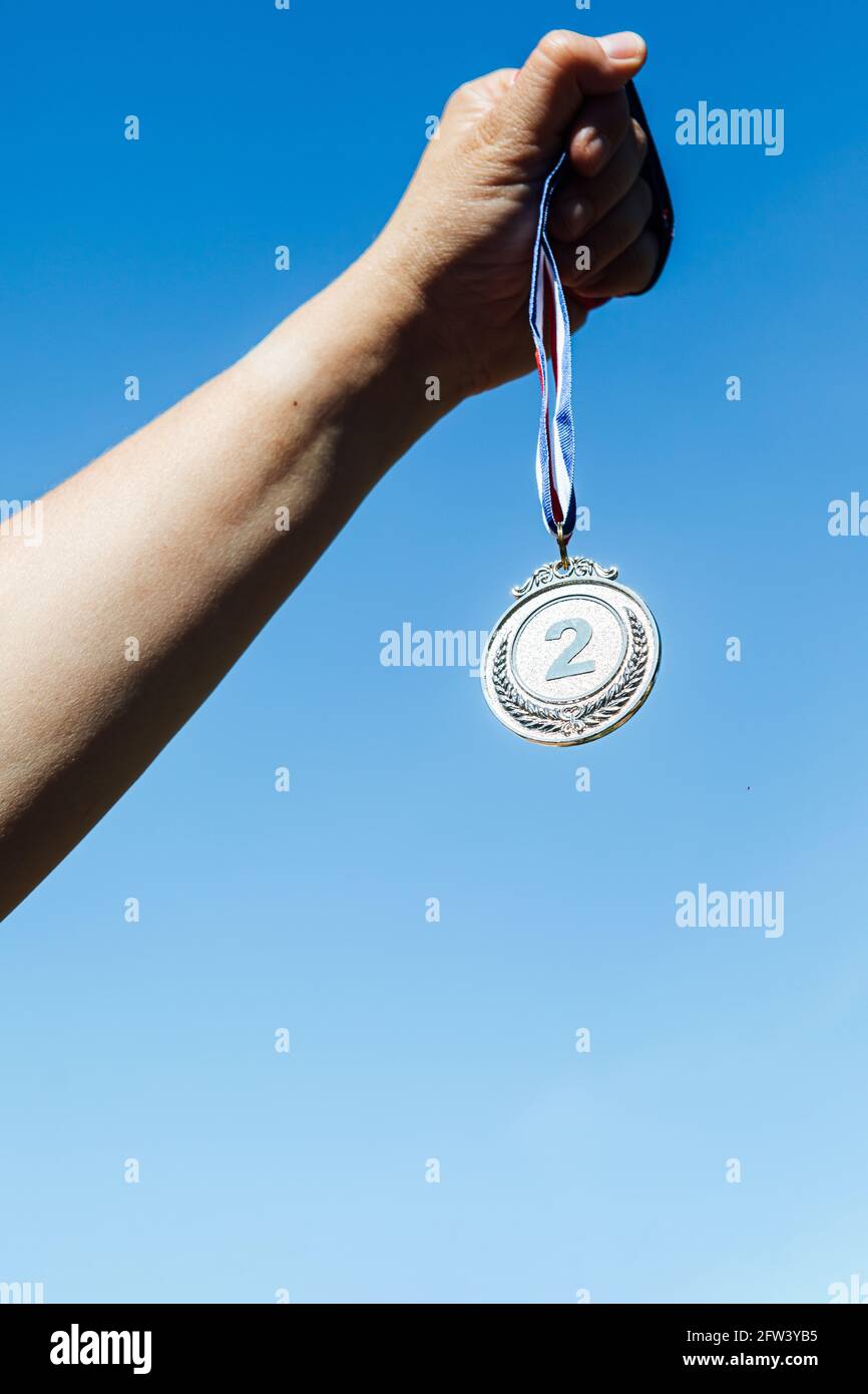 Une main tient une deuxième place de médaille d'argent, avec le ciel en arrière-plan. Concept de victoire Banque D'Images