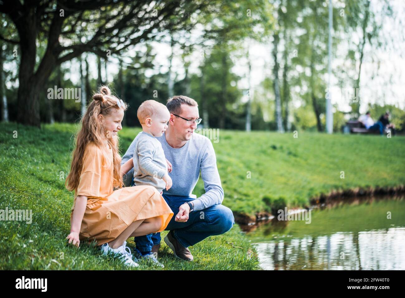 famille heureuse sur la rive près de la rivière en été dans le parc. Concept de vacances en famille dans la nature. Père et enfants, fête des pères Banque D'Images