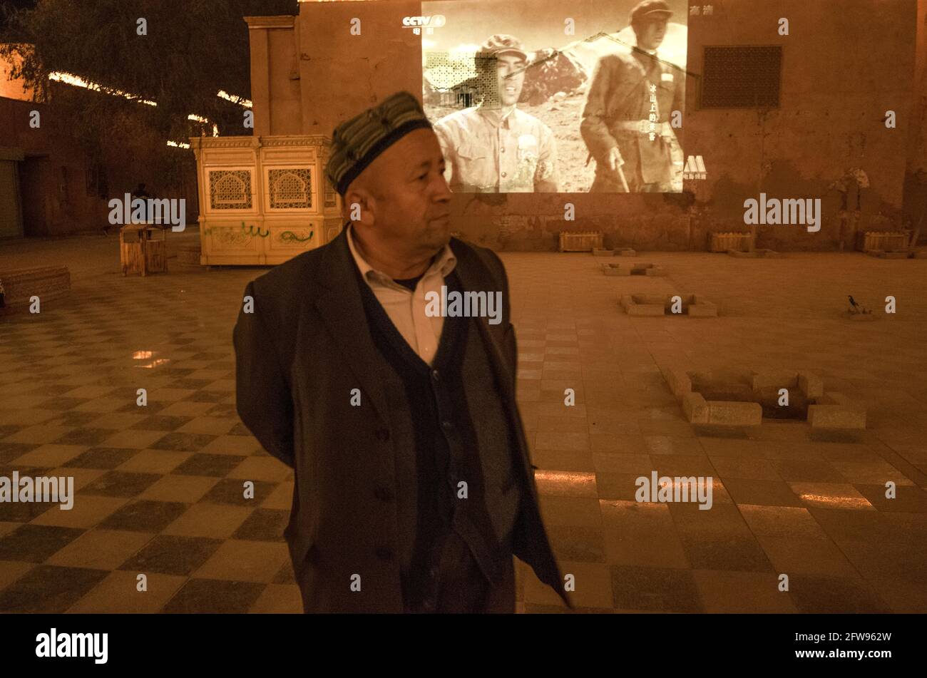 Uyhgur man au premier plan devant la caméra Alors que derrière un film noir et blanc sur les Chinois La révolution est affichée sur un écran.Kashgar 2019 Banque D'Images